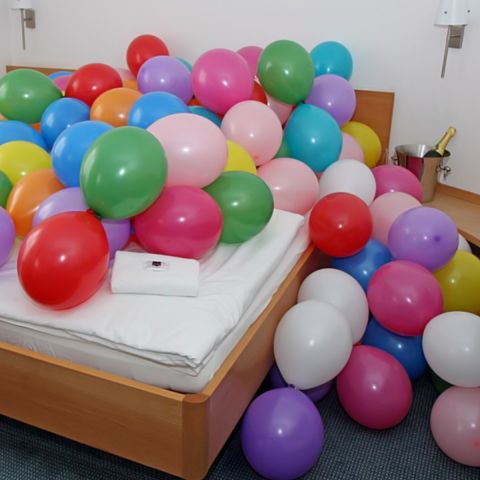 Viele bunte Luftballons, verteilt auf einem Bett oder im Schlafzimmer.